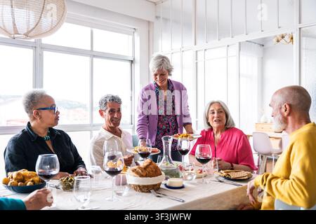 Groupe divers de personnes âgées partageant un repas et profitant de conversations à une table à manger, célébrant l'amitié, la communauté et les réunions sociales dans Banque D'Images
