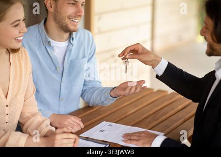 Un agent immobilier qui donne les clés de la nouvelle maison à un couple heureux et marié à la table à l'extérieur Banque D'Images