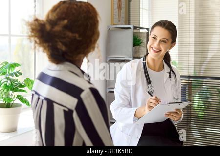 Médecine souriante consultant une patiente avec un tableau de bord lors d'un rendez-vous à la clinique Banque D'Images