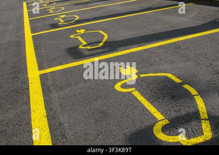 Vue en perspective d'une rangée de places de stationnement réservées vides pour véhicules électriques. Prise de vue en contre-plongée de symboles de prise de courant pour voiture électrique peints en jaune Banque D'Images