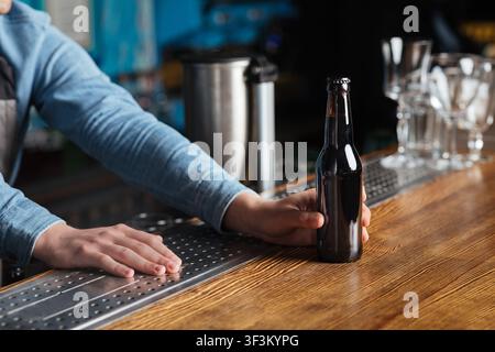 Détendez-vous dans le pub. Le barman donne une bouteille de bière sans étiquette au client sur le comptoir du bar Banque D'Images