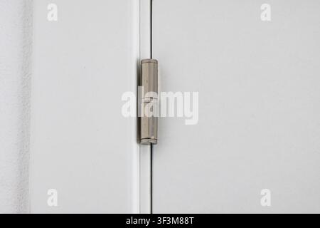 Une vue détaillée d'une charnière de porte métallique élégante reliant deux panneaux blancs, mettant en évidence son design fonctionnel Banque D'Images