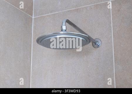 Une vue rapprochée d'un pommeau de douche chromé élégant et contemporain avec plusieurs jets d'eau, installé contre une surface carrelée beige neutre Banque D'Images
