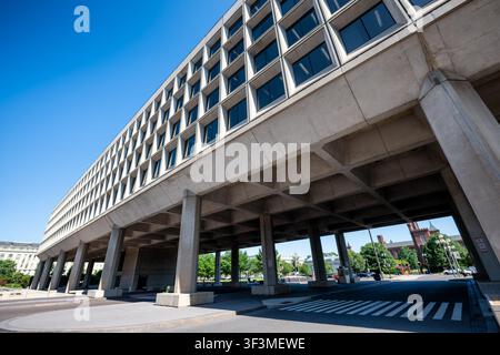 Bâtiment Forrestal sur pilotis à Washington DC | WASHINGTON D.C., États-Unis — Le bâtiment James V. Forrestal enjambe la 10e rue SW sur d'énormes piles en béton, sa masse brutaliste encadrant une vue lointaine du château du Smithsonian. Les planificateurs avaient autrefois prévu que cette axe relie le réaménagement moderniste du Southwest au Smithsonian, mais le département de la Marine a construit cette structure unique à travers la promenade au lieu de deux tours reliées, ne laissant aujourd'hui que la pointe du château visible au-dessus de la ligne du toit. Banque D'Images