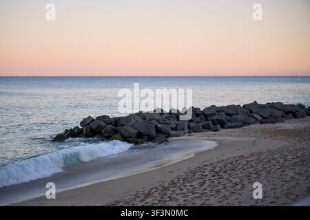 Des vagues douces se brisent sur une plage rocheuse au crépuscule Banque D'Images