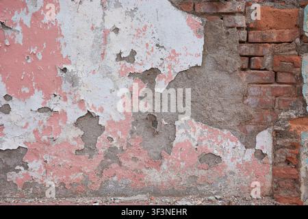 Texture de vieux mur avec peinture rose écaillée, plâtre fissuré et brique rouge apparente Banque D'Images