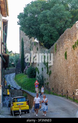 Florence, Toscane, Italie. 28 mai 2026. - Un couple se promène dans une rue étroite et ensoleillée bordée par une ancienne fortification en pierre dans la Toscane, en Italie. Banque D'Images