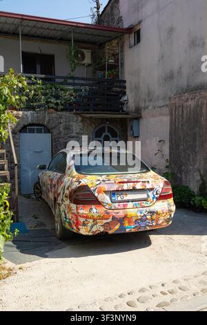 Podgorica, Monténégro. 20 juillet 2026. Une voiture est recouverte d’un film adhésif coloré et complexe représentant de nombreux personnages de dessins animés. Le véhicule est garé Banque D'Images