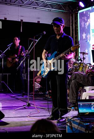 Un senior actif portant une casquette jouant une guitare électrique bleue sur une scène illuminée avec les membres de son groupe en live au Ong Ang Canal The River of Lif Banque D'Images