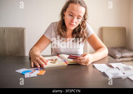 Femme gérant les finances du foyer, tenant une carte de crédit et des pièces de monnaie, l'air stressée par les factures Banque D'Images