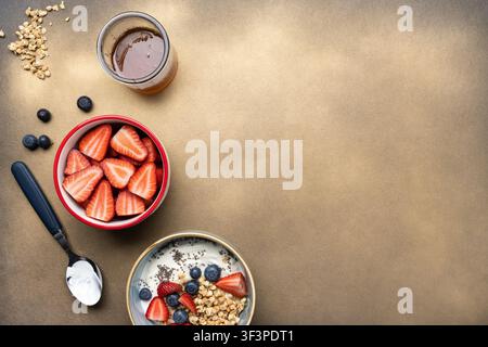 Composition minimale pour le petit-déjeuner mettant en vedette du yaourt avec granola, des fruits rouges frais, du miel et des fraises supplémentaires sur un fond beige chaud avec un espace généreux pour le texte Banque D'Images