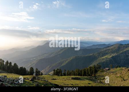 Une vue panoramique du paysage des montagnes de l'Himalaya superposées avec la chaîne Dhauladhar enneigée et un pré herbeux en premier plan sous un ciel nuageux. Banque D'Images