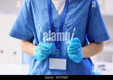 Professionnel de santé en blouse bleue et gants tenant une fiole de vaccin et une seringue, soins de santé et immunisation Banque D'Images