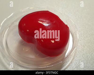 Une photographie en gros plan d'un dessert à la gelée rouge vif en forme de cœur reposant dans un récipient en plastique transparent. La gelée est lisse, brillante et translucide Banque D'Images
