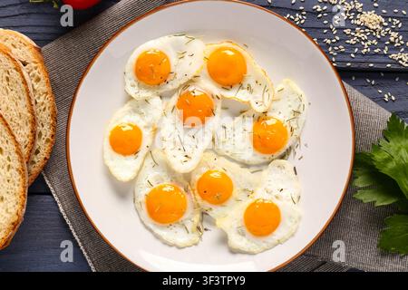 Assiette avec des œufs de caille frits, de la persil et des tranches de pain sur un fond en bois bleu Banque D'Images