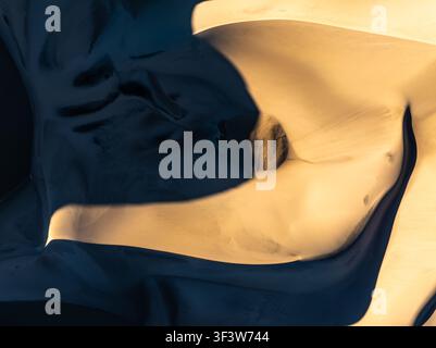 Fond de nature abstrait en gros plan montrant des motifs de dunes de sable lisses et des courbes fluides, avec des reflets dorés chauds et une ombre profonde, idéal pour le design Banque D'Images