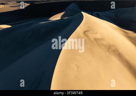 gros plan d'une crête de dune de sable doré du désert avec des courbes étendues, une ombre profonde et des textures de sable fin, créant un fond naturel abstrait avec Banque D'Images