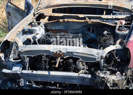 Un plan rapproché horizontal se concentrant directement sur le compartiment moteur complètement brûlé et fondu d'une épave de voiture détruite. Banque D'Images