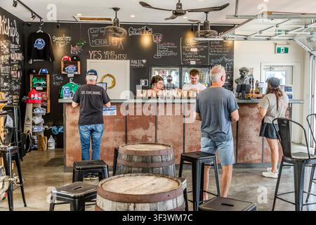 Les invités font la queue au bar de la Lightship Brewery sur Tannery Road à Lunenburg, en Nouvelle-Écosse, tandis que le personnel sert des dégustations de bière. Des pulls, des T-shirts et des casquettes de la brasserie sont exposés à la vente sur le mur, et des planches posées sur les tonneaux servent de menu des boissons. Lunenburg, Nouvelle-Écosse, Canada Banque D'Images