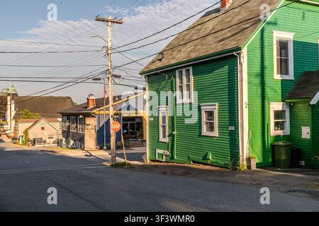 Une maison en bois peinte en vert se dresse à une jonction en pente dans la vieille ville de Lunenburg, en Nouvelle-Écosse, avec d'autres bâtiments résidentiels et commerciaux historiques visibles en arrière-plan, en descendant la colline vers le port. Les rues étroites et en terrasses font partie de l'aménagement urbain en grille que les arpenteurs britanniques ont conçu en 1753 pour la colonie fondatrice. Lunenburg, Nouvelle-Écosse, Canada Banque D'Images