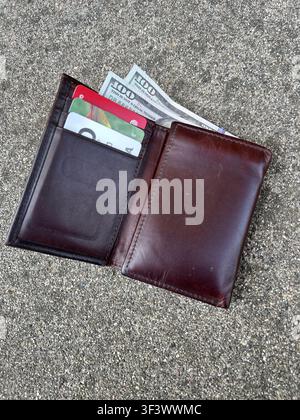 Un portefeuille en cuir marron pour homme avec de l'argent et des cartes gît sur un trottoir. Banque D'Images