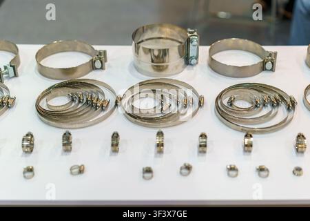 Close-up de différentes tailles de pinces à tuyau en acier inoxydable et de fixations métalliques disposées soigneusement sur une table d'exposition blanche. Banque D'Images
