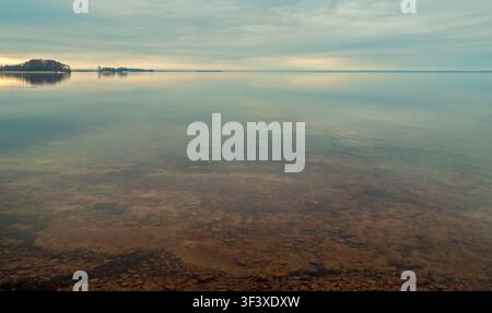 Scène tranquille de lac en Finlande avec une eau claire et peu profonde sur un lit rocheux sous un ciel doux et nuageux avec des îles au loin Banque D'Images