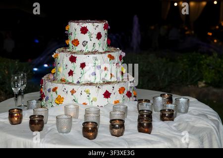 Un grand gâteau à trois étages décoré de fleurs colorées, de bougies et de verres à champagne Banque D'Images