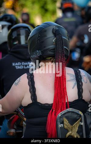 Valmiera, Lettonie - 24 juillet 2026 : Vue arrière d'une motarde tatouée portant un casque noir avec de longues tresses rouges tout en participant à un événement public Banque D'Images