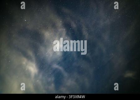 Vue grand angle d'un ciel nocturne sombre rempli d'innombrables étoiles. Des nuages translucides dérivent à travers l'étendue, illuminés par une source de lumière invisible, c Banque D'Images