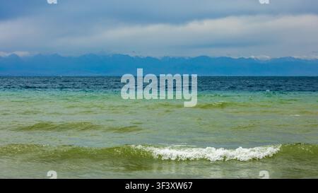 Paysage naturel vaste mettant en scène une eau de lac tranquille et des montagnes lointaines. Un ciel couvert ajoute une atmosphère dramatique à la scène sereine. Banque D'Images