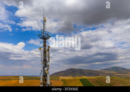 La tour de communication se dresse fièrement au milieu de collines ondulantes et de champs agricoles. Le ciel nuageux ajoute une touche dramatique au paysage vaste et isolé, mettant en valeur Banque D'Images