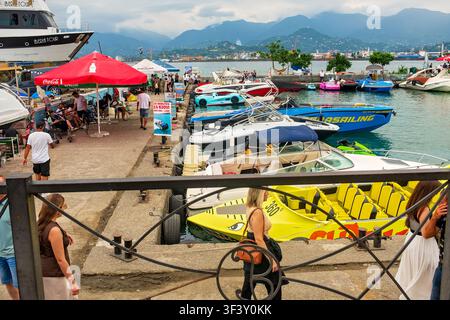 Batumi, Géorgie - 19 juillet 2026 : Vue sur le front de mer animé avec des hors-bords amarrés dans le port et des gens marchant le long de la jetée Banque D'Images