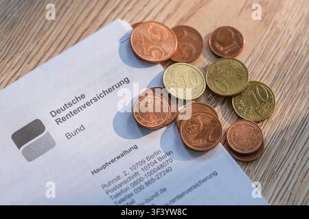 Un gros plan d'un en-tête de la Caisse fédérale de retraite allemande sur une surface en bois, sur laquelle repose un petit tas de pièces en euro Banque D'Images