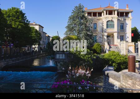 Statue debout dans le canal de la Sorgue avec le bâtiment de la Caisse d'Épargne et des présentations florales à L'Isle-sur-la-Sorgue, France. Banque D'Images