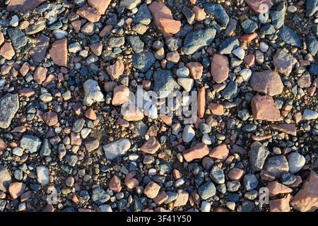 Texture d'une route rurale avec du sable, des cailloux et du gravier concassé. Surface de gravier naturel et fond géologique. Pierres de granit mélangées sur une route côtière Banque D'Images