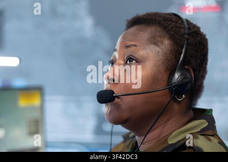 Grossissement d'un officier de communication portant un casque et regardant des images satellite sur des écrans. Dispatchère militaire féminine coordonne une opération depuis un poste de travail de surveillance Banque D'Images