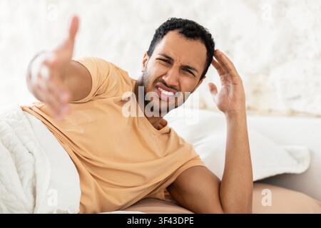 Jeune homme frustré à la peau foncée allongé dans son lit, se sentant fatigué, concept de routine matinale Banque D'Images