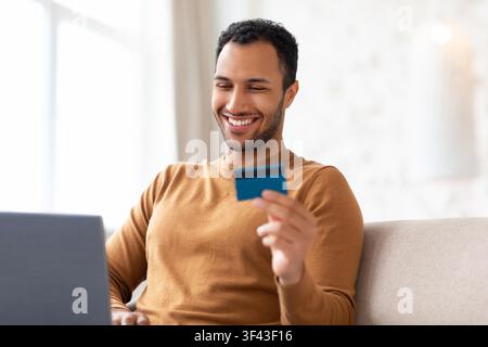 Homme heureux tenant une carte de crédit pour des achats en ligne à la maison, concept commercial Banque D'Images