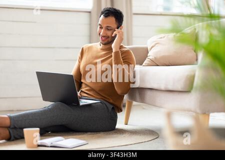 Homme noir souriant travaillant sur un ordinateur portable et téléphonant à domicile, concept d'affaires Banque D'Images
