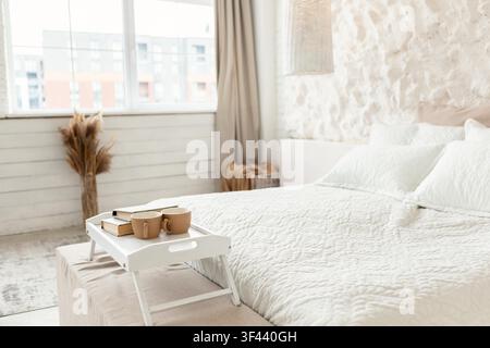 Chambre confortable avec lit blanc et plateau de café et de livres, design d'intérieur moderne Banque D'Images