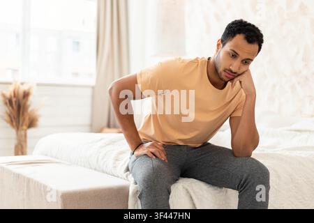 Jeune homme pensif assis sur un lit, l'air pensif dans la chambre, concept de santé mentale Banque D'Images