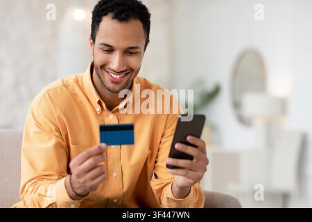Homme heureux tenant une carte de crédit et un smartphone à la maison, concept de shopping en ligne Banque D'Images
