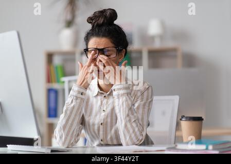 Jeune femme caucasienne stressée se frottant les yeux au bureau dans un bureau, surmenée et fatiguée Banque D'Images