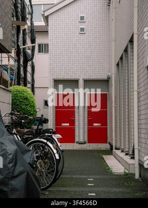 Deux portes d'entrée rouges d'un immeuble d'appartements résidentiels avec des vélos garés dans une ruelle étroite, Japon Banque D'Images