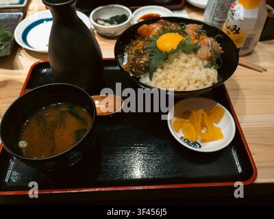 Bol de riz au sashimi de saumon Kaisendon avec jaune d'œuf cru, soupe miso, cornichons et saké servis sur un plateau dans un restaurant de Shinjuku, Tokyo, Japon Banque D'Images