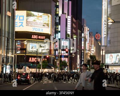 Des foules traversant une rue animée au crépuscule, entourées de panneaux publicitaires et de néons illuminés à Shinjuku, Tokyo, Japon Banque D'Images