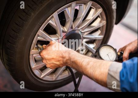 Les mains d'un mécanicien vérifient la pression des pneus d'une voiture pour la sécurité et les performances du véhicule Banque D'Images