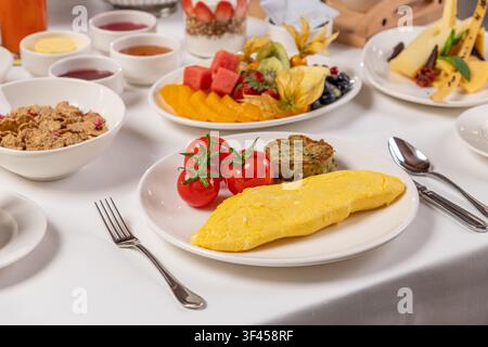 Table de brunch luxueuse avec omelette, tomates, pâtisseries, fruits et thé Banque D'Images