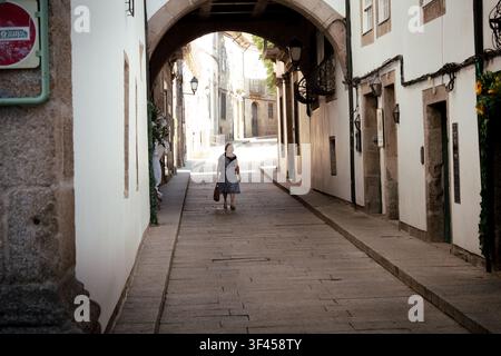 Guimarães, 26 juillet 2026 ; Femme marchant le long d'une vieille rue pavée sous une arche de pierre à Guimarães, Portugal. Banque D'Images